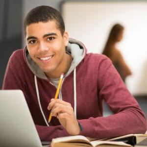 带着笔记本电脑的微笑学生坐在桌子旁 & books holding pencil